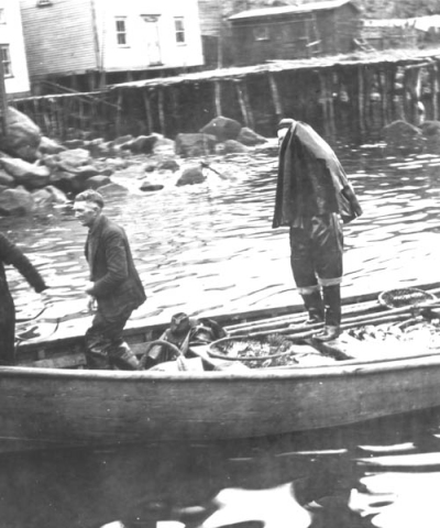 449: J V McCarthy's skiff arriving with a load of fish. J V McCarthy (left). Michael Reddy's  house at center, his father James' house at left, James' shed at right. [courtesy of  Mollie McCarthy]  - J V son of Thomas McCarthy &amp;amp; Anastasia Fitzgerald, married Julia Reddy